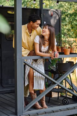 Bir erkek ve bir kadın verandada durur ve romantik kaçamakları sırasında etraflarındaki manzaranın tadını çıkarırlar..