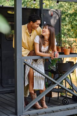 A man and a woman stand on a porch, enjoying the view of the surrounding nature during their romantic getaway. clipart