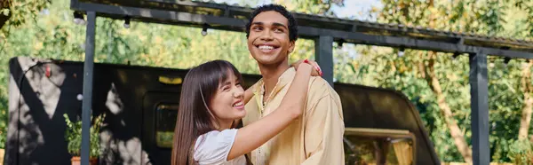 stock image An interracial couple standing side by side, enjoying a romantic moment in the serene natural environment of their camper van getaway.