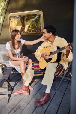 Bir erkek gitar çalarken bir kadın dikkatle dinler ve sakin bir ortamda tatlı bir müzik yaratır..