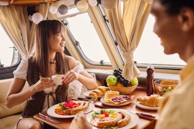 An interracial couple enjoying a delicious meal together in a cozy camper van, creating memories on a romantic getaway. clipart