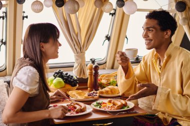 An interracial couple enjoying a delicious lunch in their camper van. clipart
