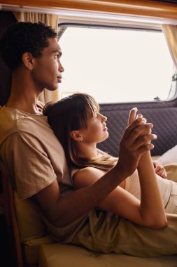 Bir erkek ve bir kadın, ırklar arası bir çift, minibüste yan yana oturur, birlikte yolculuk ederken samimi bir kucaklaşmayı paylaşırlar..