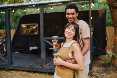 An interracial couple embraces by their camper van during a romantic getaway adventure. clipart