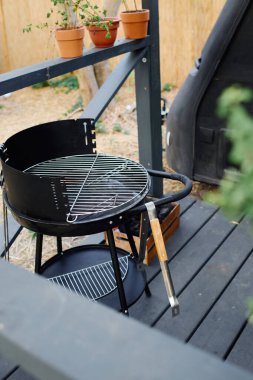 Bereketli saksı bitkileriyle çevrili ahşap bir güvertede davetkar bir barbekü sahnesi, sakin bir açık hava yemeği deneyimi yaratıyor..