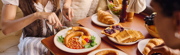 A diverse couple sit around a table, enjoying plates of food in a cozy and communal setting.
