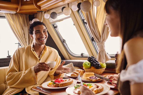 Межрасовая пара наслаждается вкусной едой вместе в фургоне кемпера, создавая воспоминания о романтическом отпуске.