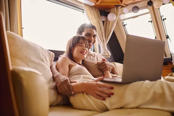 stock image A man and woman sit closely on a couch, both focused on a laptop screen in front of them.