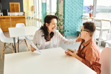 attractive happy mother in casual clothes with her inclusive son with Down syndrome holding menu clipart