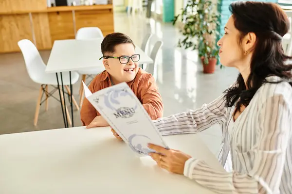 Stock image loving jolly mother sitting in cafe with her inclusive son with Down syndrome with glasses and menu