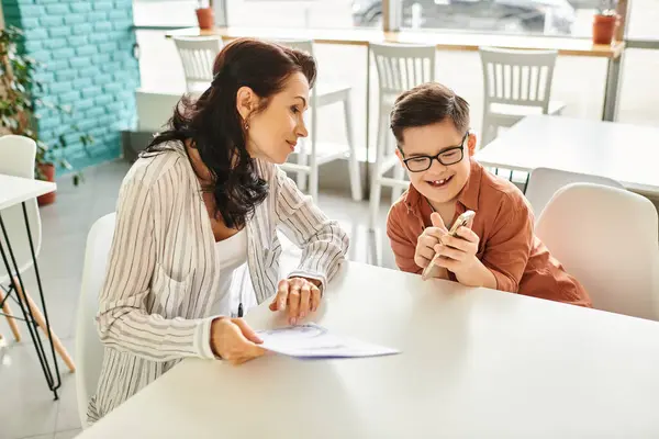 stock image good looking happy woman in casual clothes with her inclusive son with Down syndrome holding menu