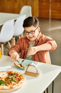 preadolescent joyous inclusive boy with Down syndrome with glasses eating pizza while in cafe clipart