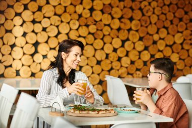 happy mother eating pizza and drinking juice with her inclusive cute son with Down syndrome clipart