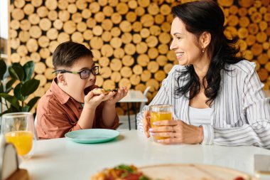 Mutlu anne pizza yiyor ve Down sendromlu yakışıklı oğluyla meyve suyu içiyor.