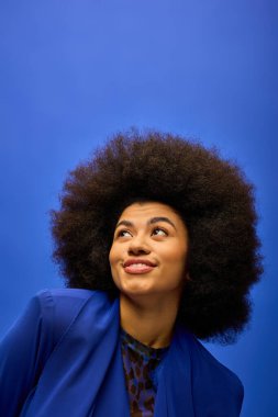 Mavi bir duvarın önünde duran kıvırcık saçlı şık Afrikalı Amerikalı kadın..