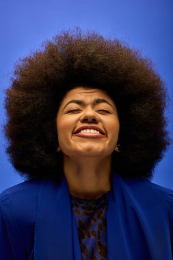 Kıvırcık saçlı, mavi ceketli ve gülümseyen Afro-Amerikan kadın..