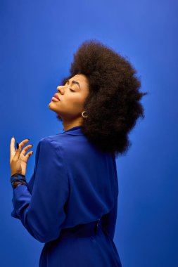 A fashionable African American woman with curly hairdohairstyle strikes a pose in a blue dress against a colorful backdrop. clipart