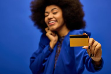 Elinde kredi kartı olan ve gülümseyen şık giyinmiş neşeli Afro-Amerikan kadın..