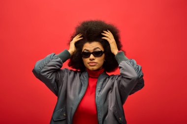 Zarif bir Afro-Amerikan kadın, renkli gölgeler ve canlı bir arka plana karşı bir ceket giyer..