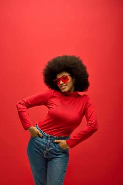 Yüzünde kırmızı güneş gözlüğü olan şık bir Afro-Amerikan kadın, canlı bir arkaplanda poz veriyor..