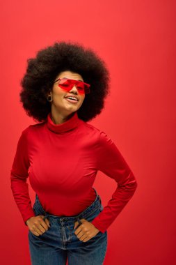 Kırmızı gözlüklü ve tişörtlü şık Afro-Amerikan kadın canlı arkaplanda poz veriyor..