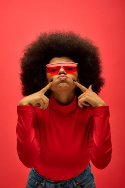 Kırmızı gömlekli ve gözlüklü şık Afro-Amerikan kadın poz veriyor..