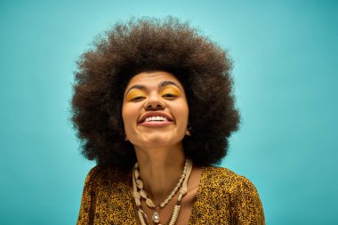 Havalı giyinmiş şık bir Afro-Amerikan kadını, ışıl ışıl bir gülümsemesi ve enfes bir afro saçı var..