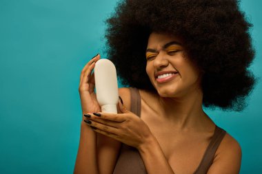 Kıvırcık saçlı, elinde saç kurutma makinesi olan şık bir Afro-Amerikan kadın..