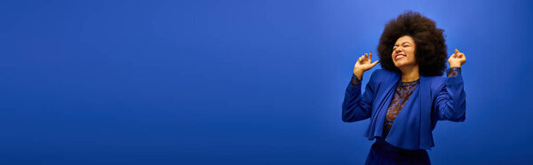 Stylish African American woman with curly hairdoposes against vibrant blue background.