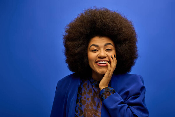 Smiling woman with curly hairdoin stylish attire, holding hand to face.