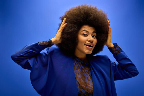 Stylish African American woman in trendy attire, holding and admiring her voluminous afro hair.