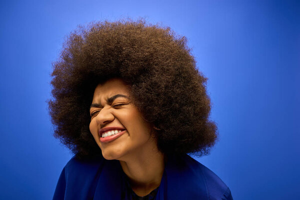 Улыбающаяся афроамериканка с кудрявой прической в стильной синей куртке.