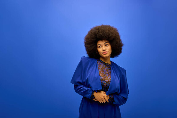A stylish African American woman with curly hairdohairstyle standing against a vibrant blue background.