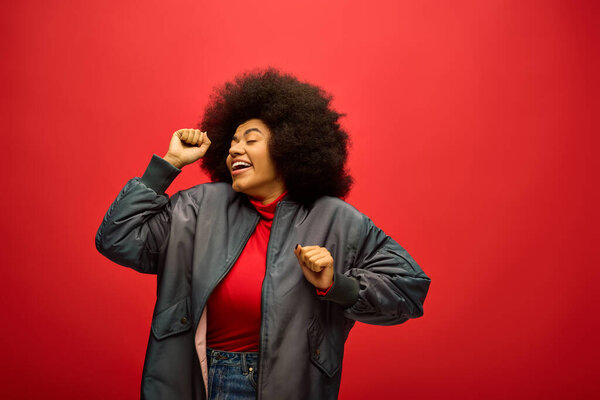 Stylish African American woman with curly hairdoposing in front of a vibrant red backdrop.