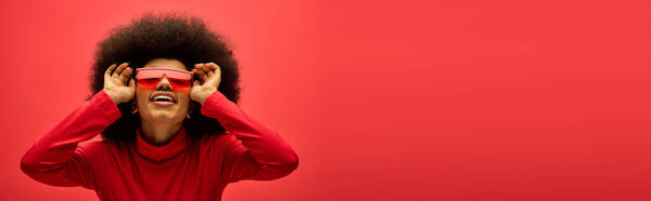 Африканская американка уверенно носит красную рубашку и одинаковые очки.