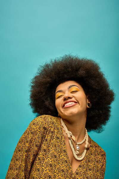 A stylish African American woman with curly hairdois smiling on a vibrant backdrop.