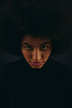 Büyük afro saçlı modaya uygun Afro-Amerikan kadın kameraya özgüvenle bakıyor..