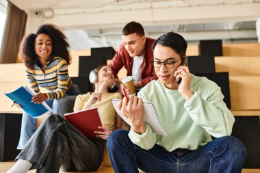 Çok kültürlü öğrenciler yerde oturuyor, telefon konuşmalarına dalmış, eğitim ortamında bağlantıları teşvik ediyorlar.
