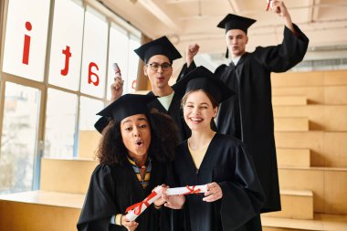 Mezuniyet elbiseleri ve şapkaları içindeki çok kültürlü öğrenciler akademik yolculuklarını tamamladıktan sonra mutlu bir şekilde resim için poz veriyorlar..
