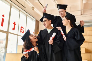 Mezuniyet elbiseleri içinde diploma taşıyan mutlu öğrencilerden oluşan çok kültürlü bir grup..