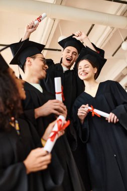 Mezuniyet elbiseleri ve kepleri içinde bir grup farklı öğrenci akademik başarılarını kutlamak için bir arada duruyorlar..