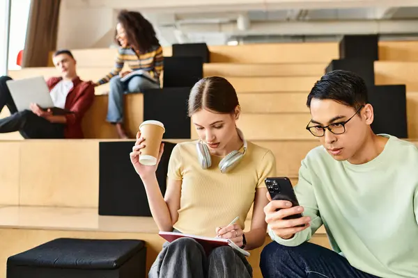 stock image A man and a woman, both students, sit on steps, engaged as they look at a cell phone together