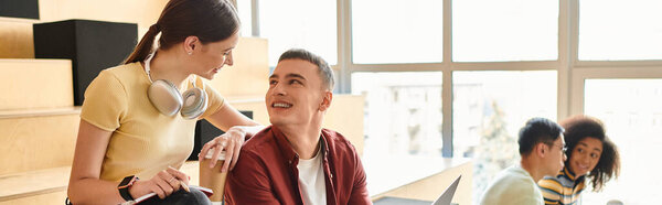 Группа мультикультурных студентов, включая афроамериканку, сидят за столом, работая над своими ноутбуками.