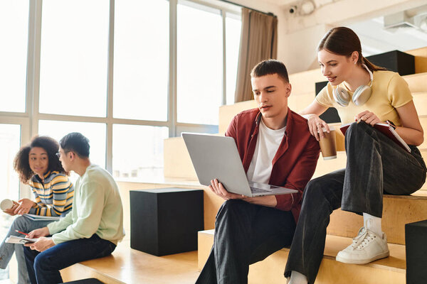 A group of students from various backgrounds sitting and conversing on a colorful set of stairs indoors