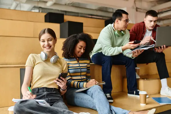 stock image A diverse group of students, including a black girl, enjoy music while sitting on steps with headphones on.