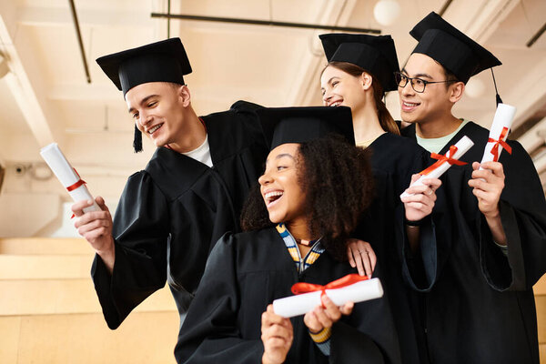 Multicultural group of happy graduates in gowns holding diplomas.