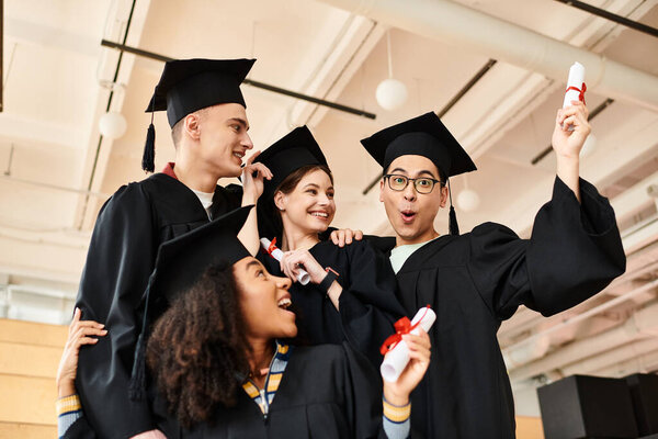 Diverse group of students in graduation gowns and caps happily taking a selfie together.