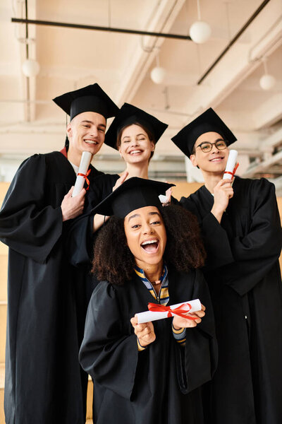 A diverse group of happy students in graduation gowns posing for a picture indoors.