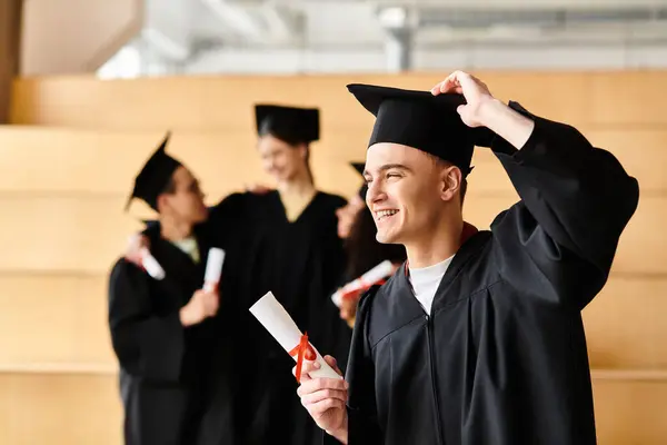 stock image A diverse man, clad in a graduation cap and gown, proudly holds a diploma with a beaming smile, signifying academic success.