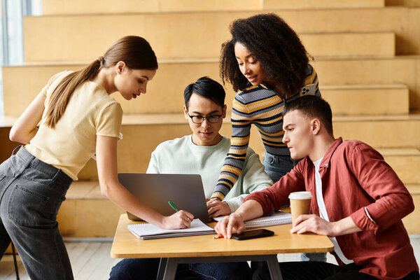 Diverse group of students focused on laptop work at table in university setting.